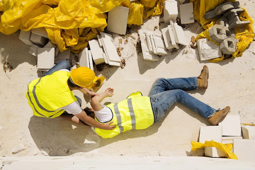 A man attends to a construction worker who has a potentially broken arm after a work accident, which could be a cause for a workers’ compensation claim.