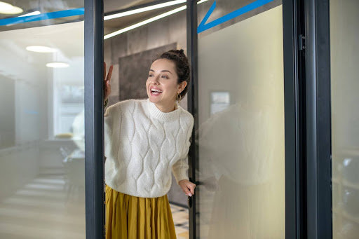 A young employee sticking her head into the boss’s office at the start of the workday; clear communication to avoid wage and hour violations. 