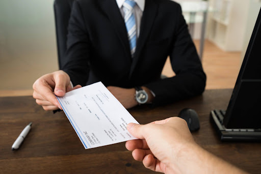 Business professional handing an employee a paycheck across a desk, representing wage and hour laws, payroll compliance, employee compensation, and trends to watch.