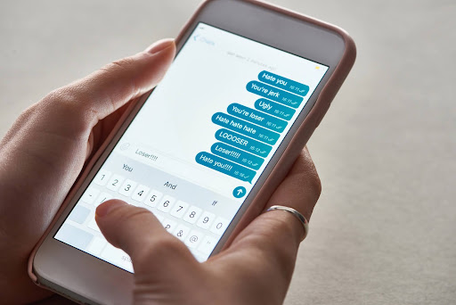 Person holding a smartphone displaying hostile text messages, representing anonymous harassment complaints and workplace harassment investigations.