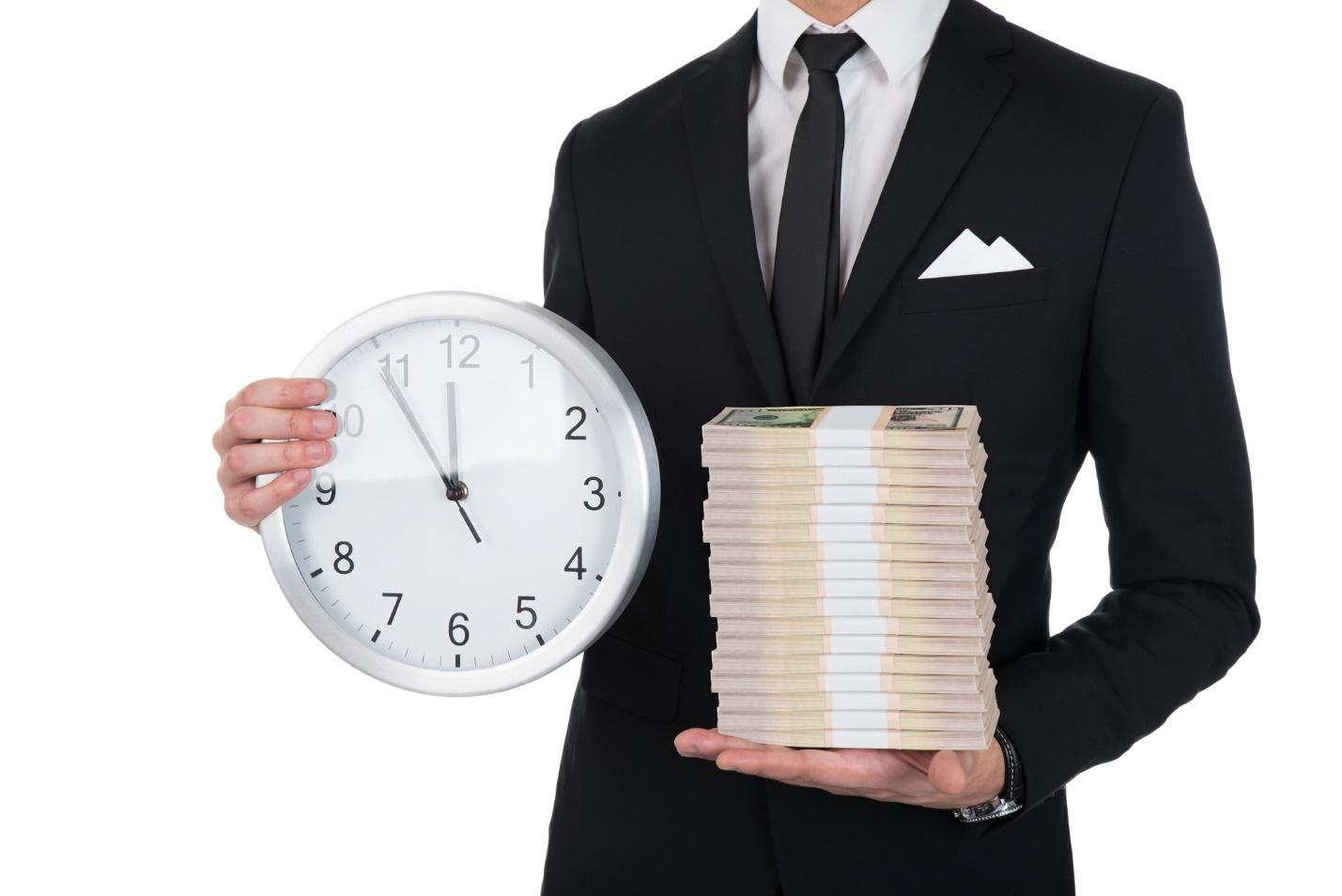 An attorney in a black suit holds a clock in his right hand and a stack of paper money in his left hand after successfully winning wage and hour claims due to employee contracts.