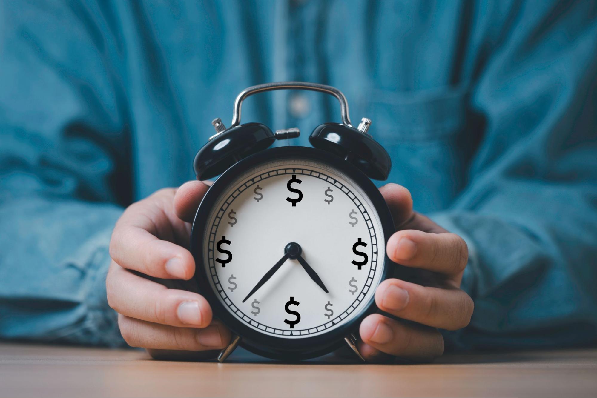A man holds an alarm clock filled with dollar signs as he deals with the comp time for non-exempt employees