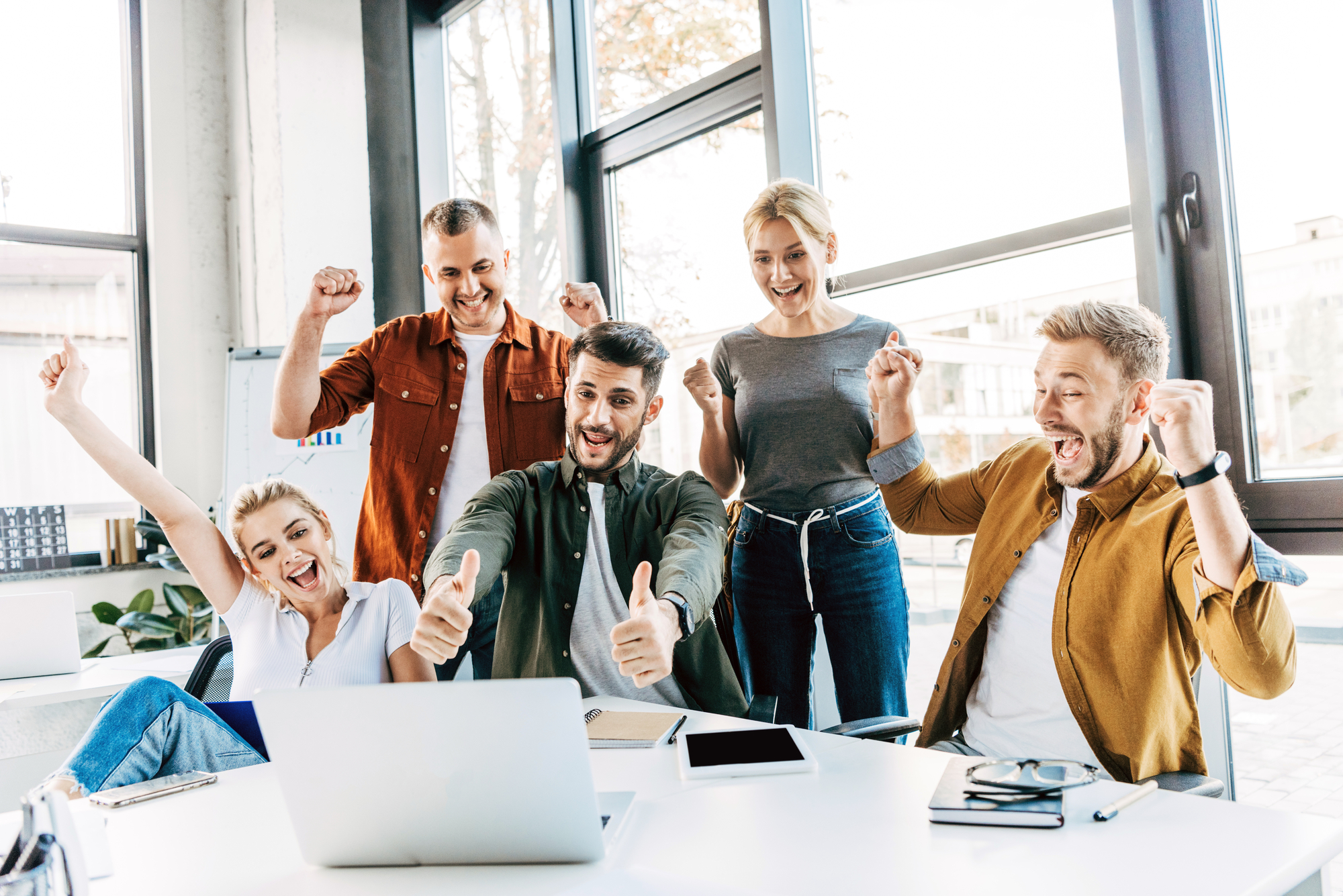 Small business team in casual attire gathered around a laptop, celebrating; company culture concept. 